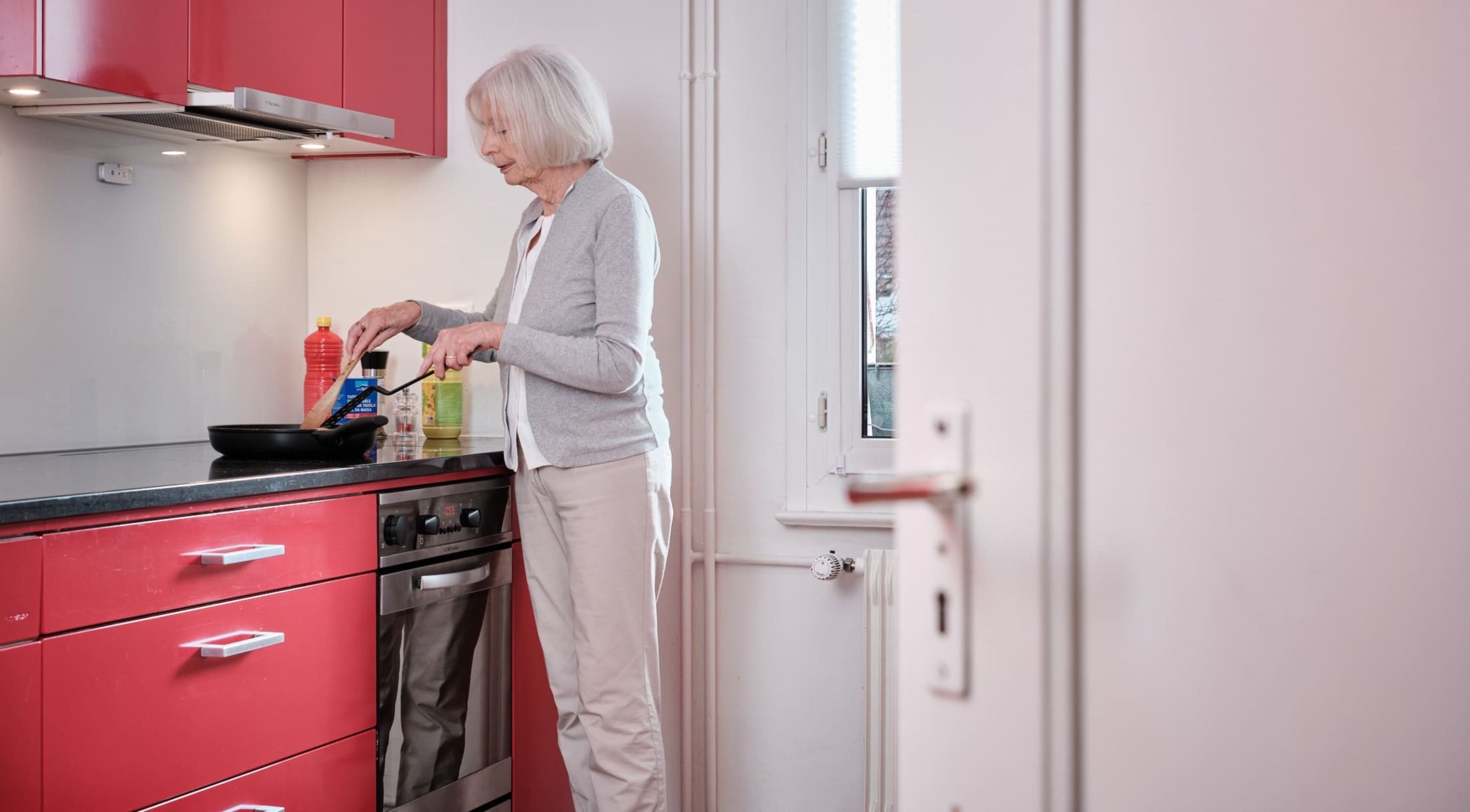 Une personne âgée est dans sa cuisine en train de cuisiner.