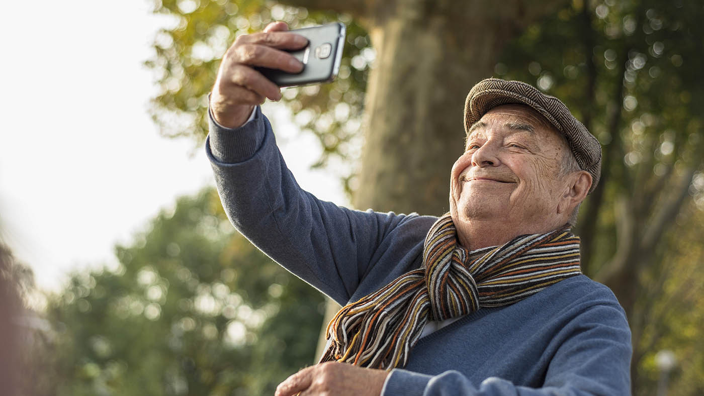 Un senior est sur son téléphone portable et prend un selfie de lui-même.