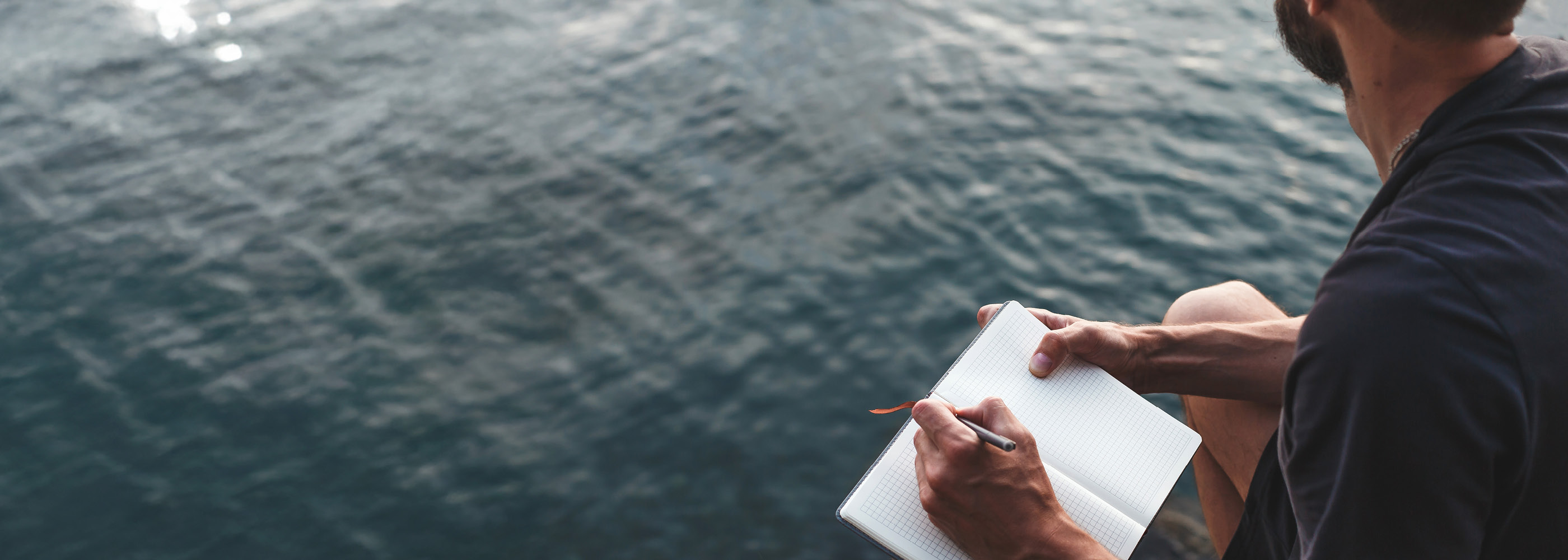 Un monsieur écrit dans un carnet en regardant le lac.